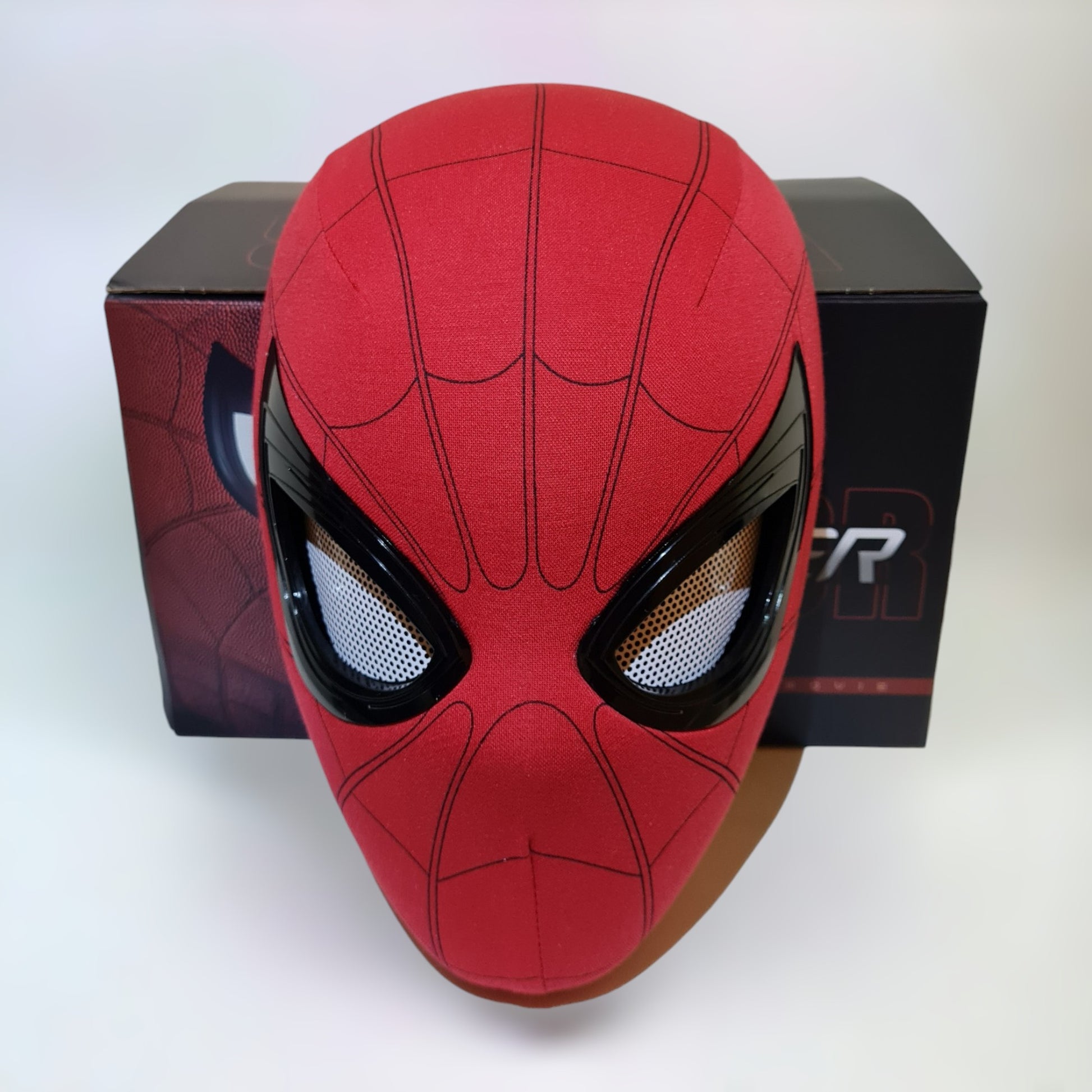 Spiderman mask blinking eyes movable remote control in front of box on a plain white background.