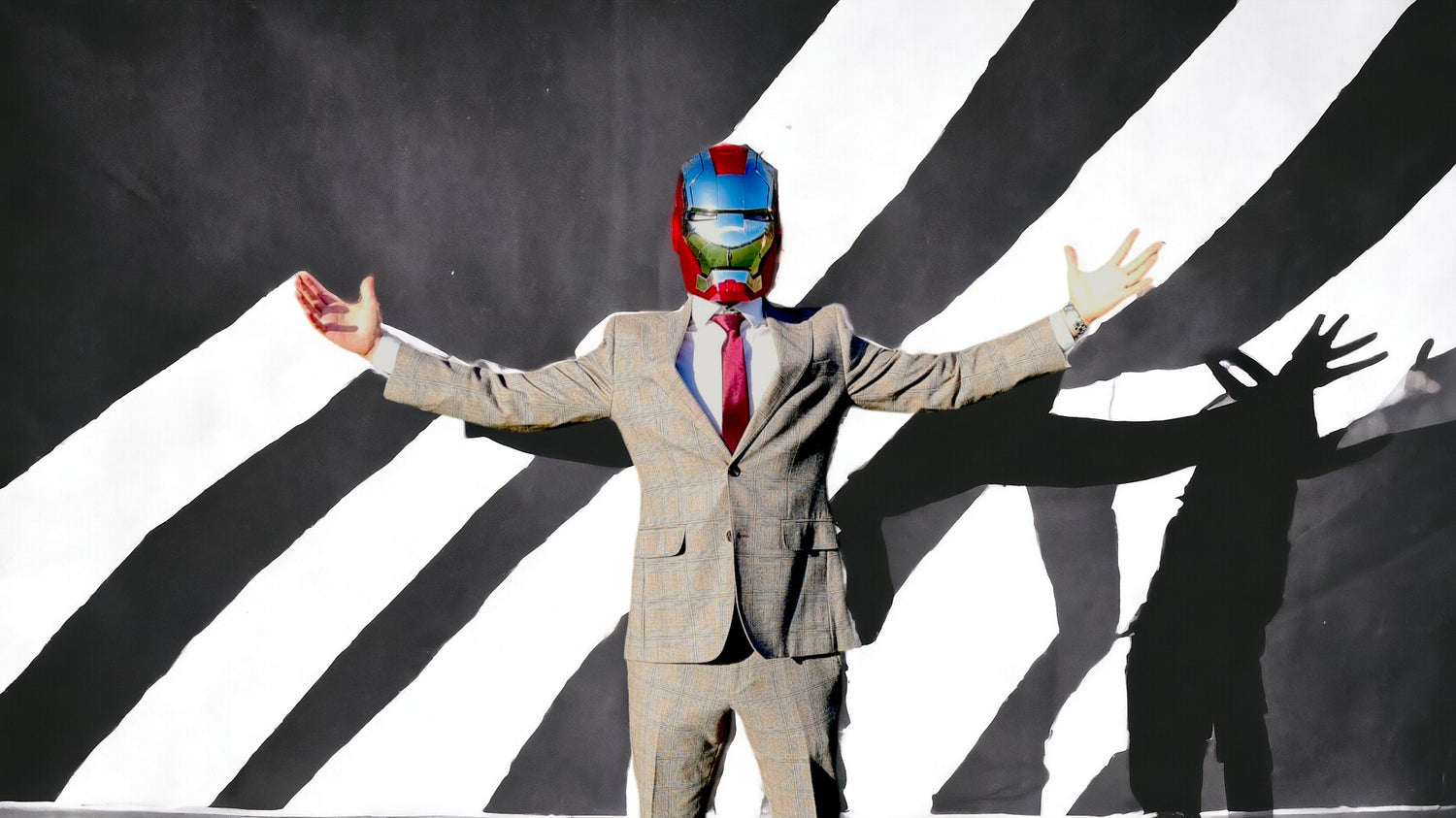 A man in a gray suit, wearing the silver Iron Man MK5 helmet with an artistic black and white background.